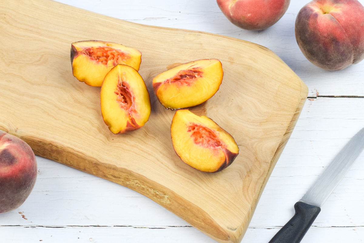 A chopping board with a quartered peach, next to 3 peaches