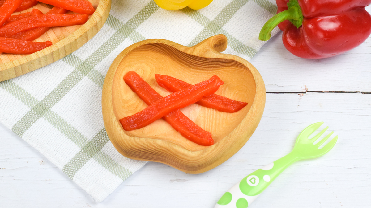 A serving of steamed red pepper next to a whole yellow and red pepper