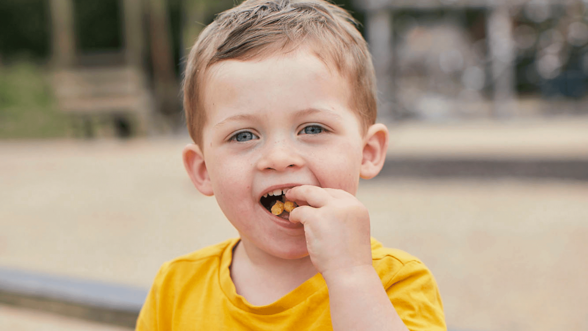 Toddler at the park wearing a yellow t-shirt and eating an Organix Toddler snack