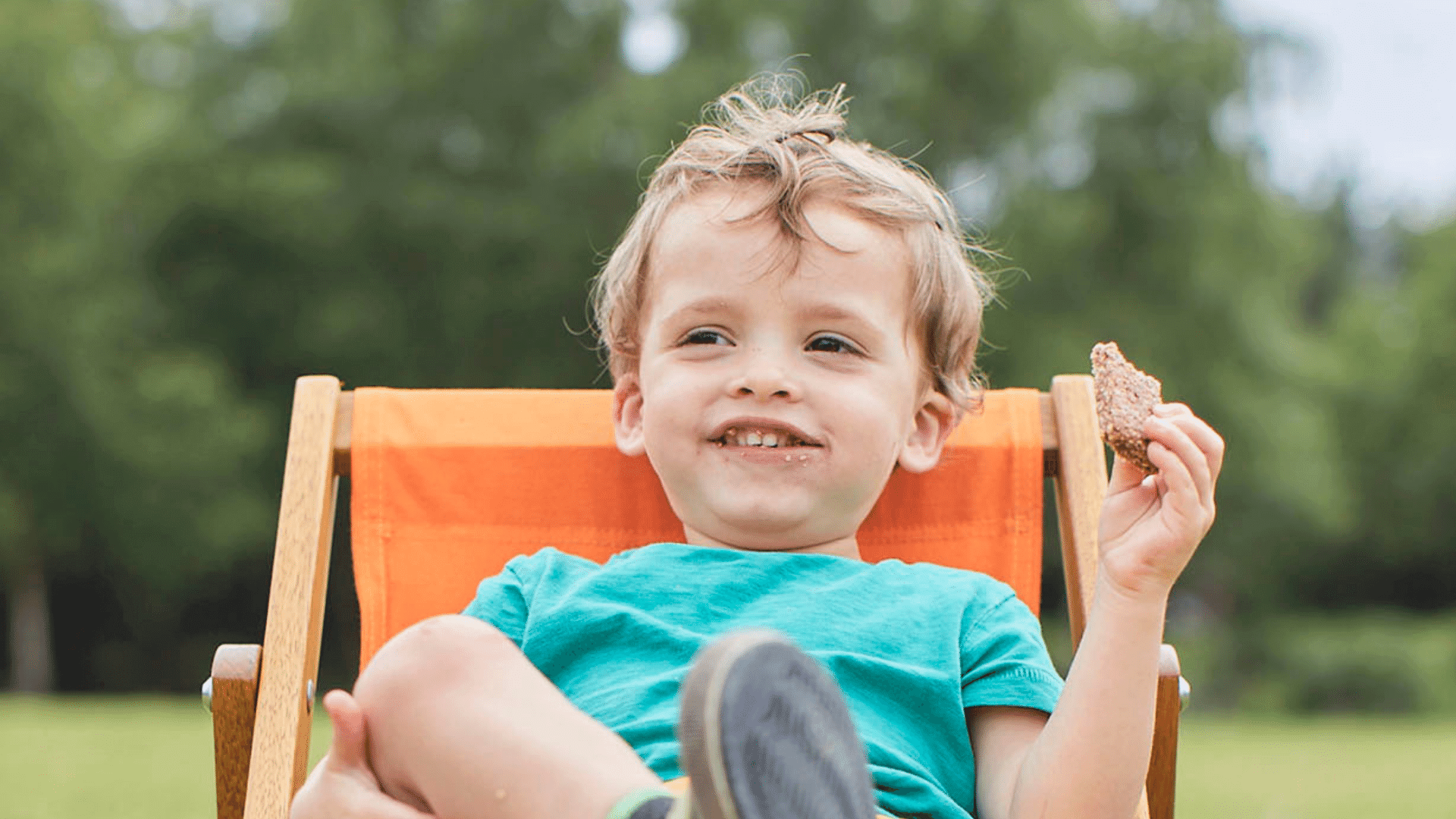 Toddler outdoors sitting on a camping chair eating an Organix oaty bar