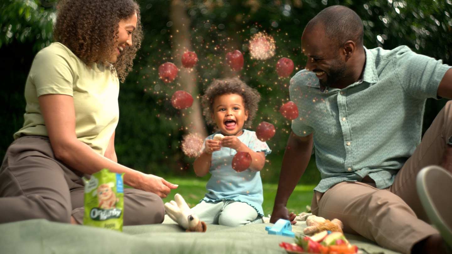 Mum dad and baby on a picnic blanket baby enjoys Organix food and experiences  a rainbow burst of flavour