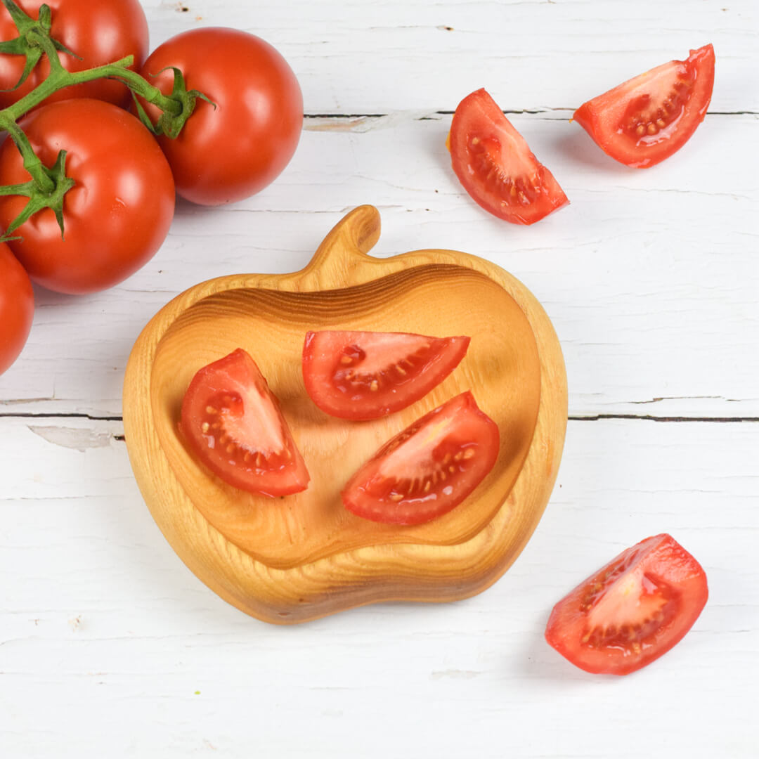 A bowl of tomato wedges next to 3 segments of tomatoes and some whole tomatoes on a vine